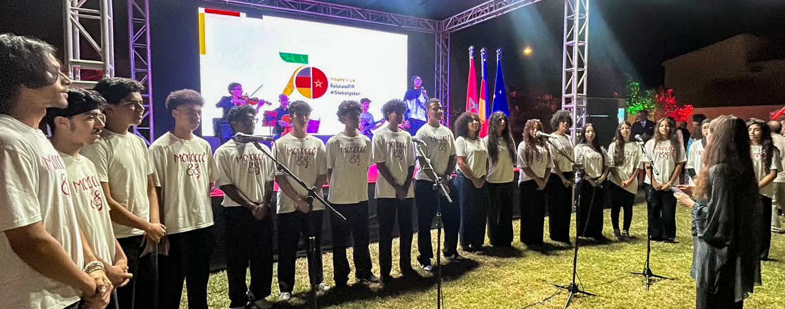 Morocco88 choir members in matching programme shirts singing together in front of an outdoor stage